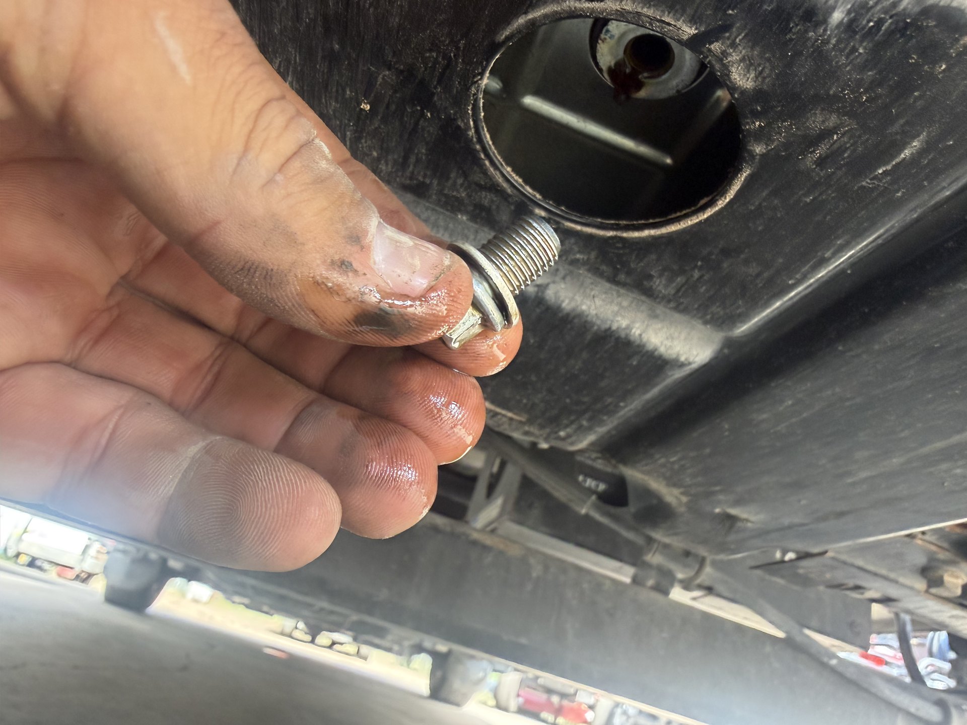 Technician holding the oil drain plug and sealing washer beneath an RV generator pan during an oil change