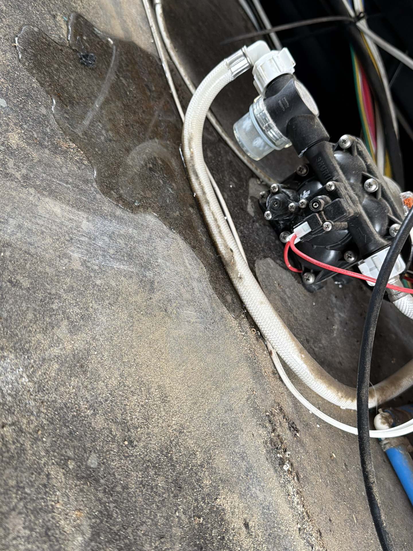 RV fresh water pump, check valve, and braided supply line connected in a tight underfloor compartment