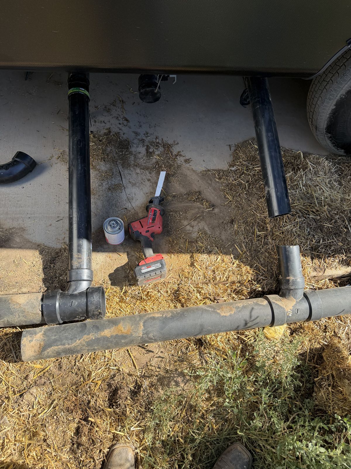 New ABS drain plumbing tees and pipe laid out under an RV undercarriage with cement and a reciprocating saw on the ground