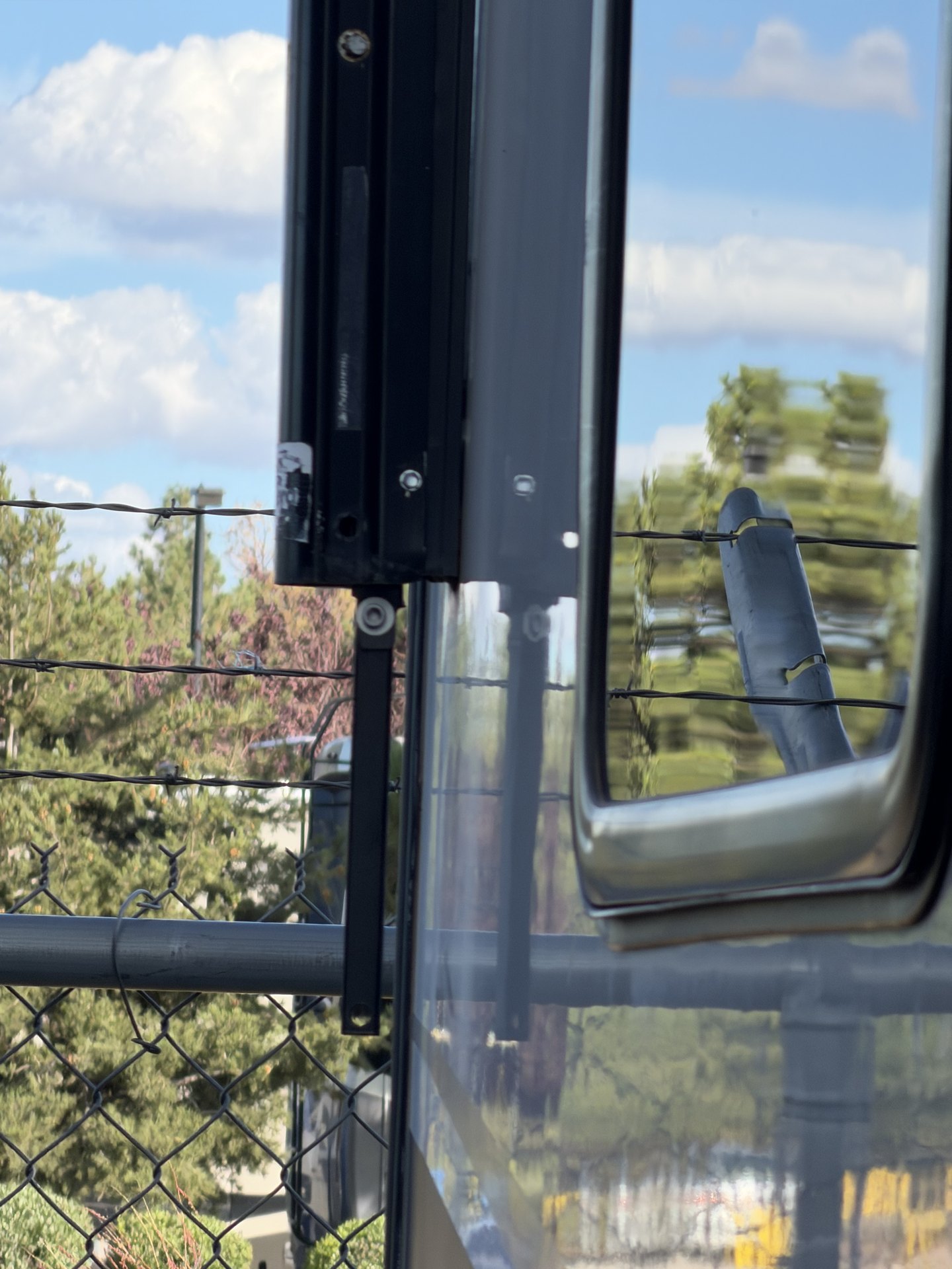 RV window frame partially open during replacement showing the black frame channel and glass against a pine and blue sky background