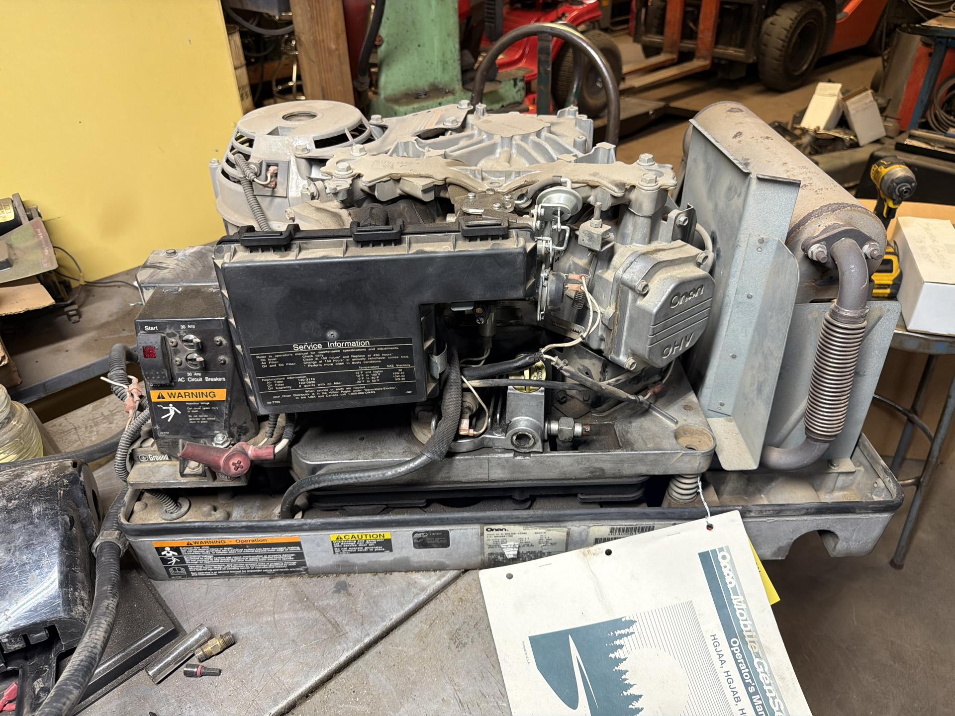 Onan RV generator set out of the coach on a shop bench with its cover removed and the operator manual alongside