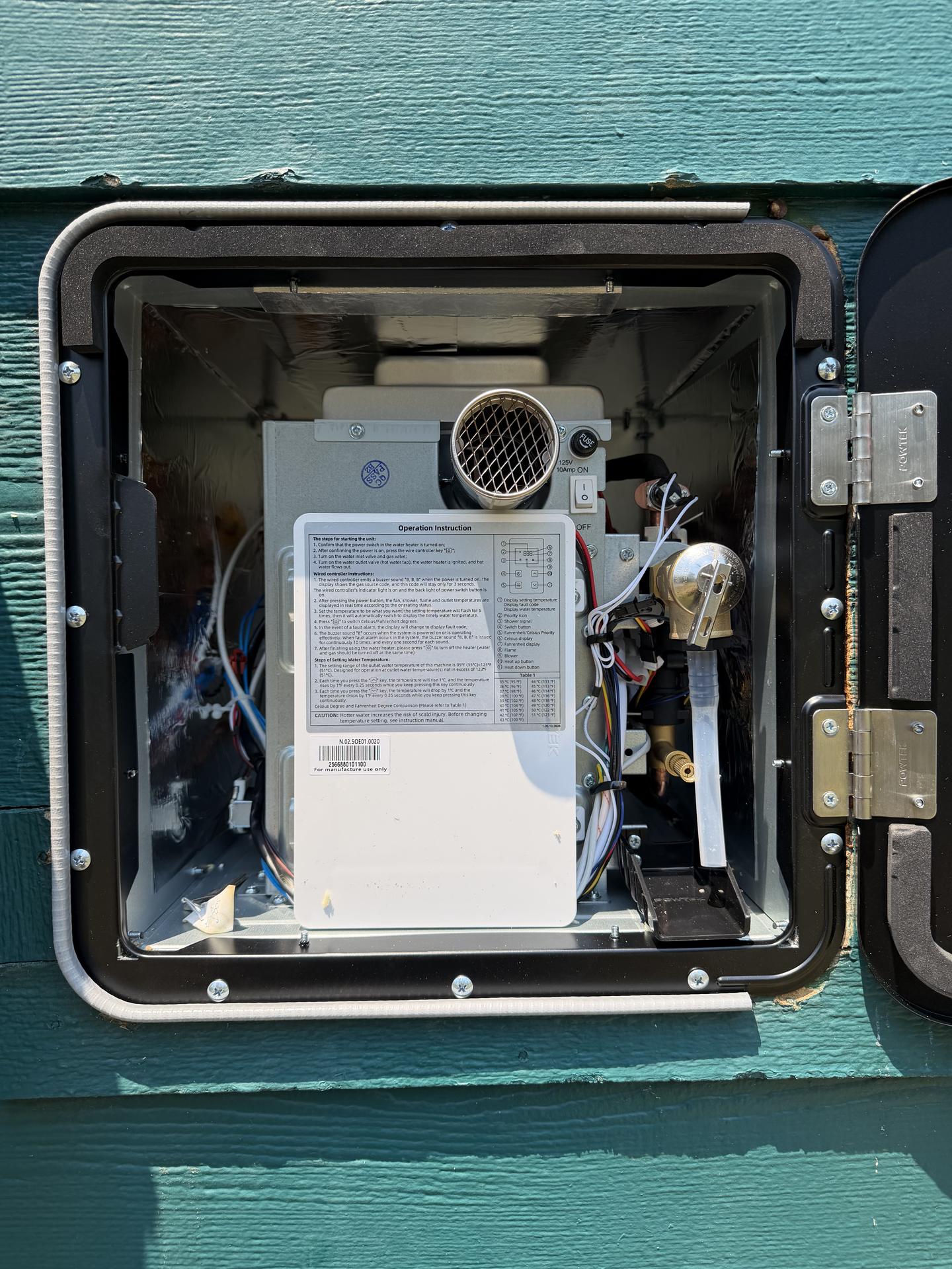 Newly installed RV tankless water heater visible through the open exterior access door with gas valve, wiring, and vent in place