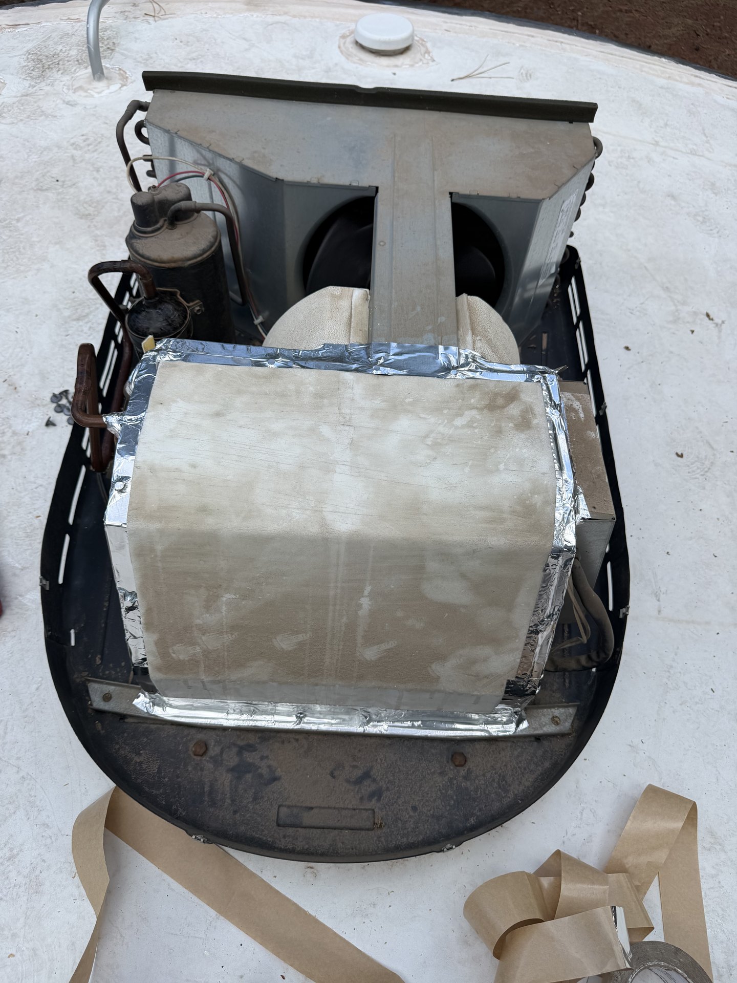 Rooftop RV air conditioner lifted off its roof opening showing the foil-taped duct box and new mounting gasket area
