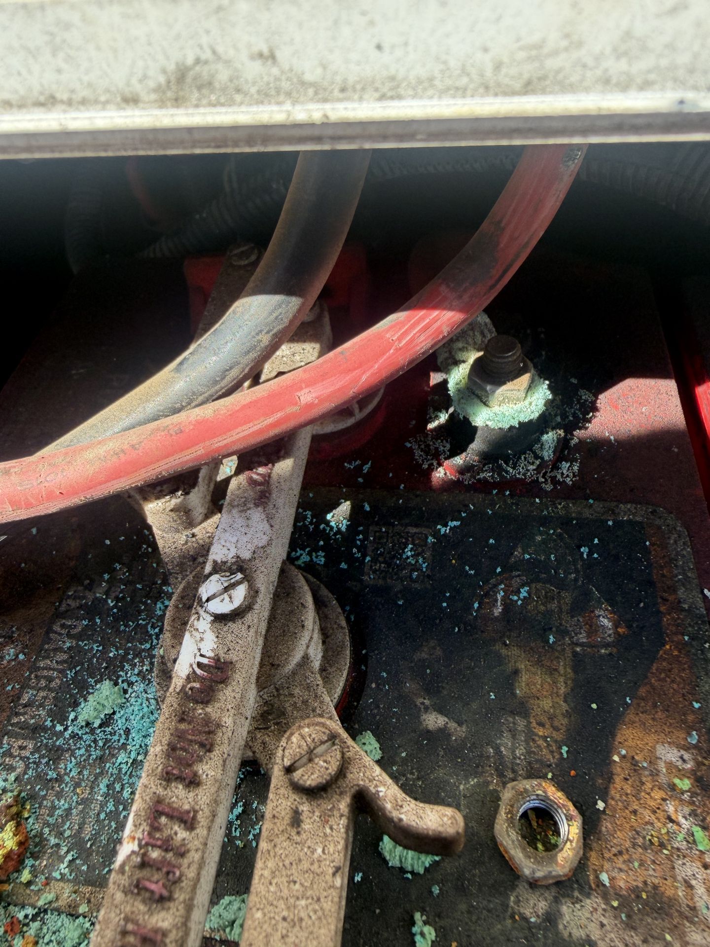 Close view of an RV battery cable lug and hardware coated in green corrosion inside the battery bay before cleanup