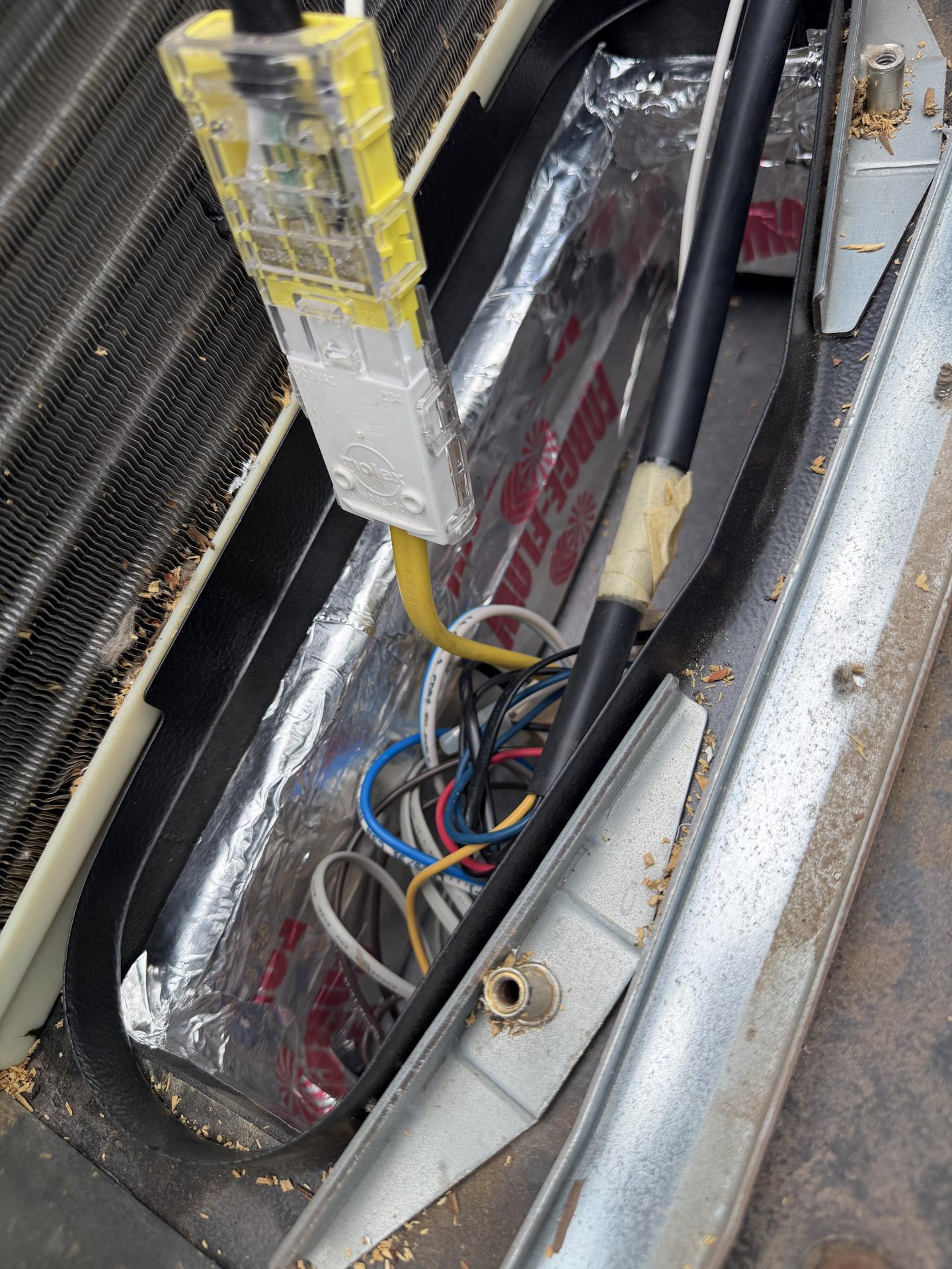 Rooftop RV air conditioner opened up showing condenser coil, wiring harness plug, and control wiring during capacitor repair