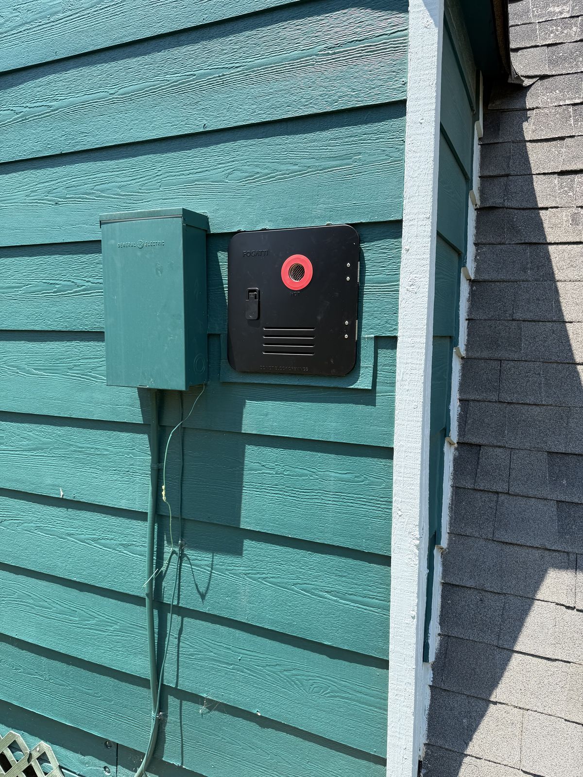Exterior RV power disconnect box and tankless water heater access door installed on a green-painted sidewall