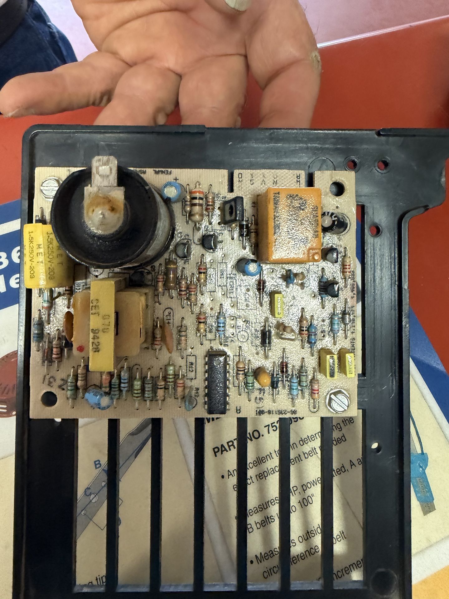Technician holding an older RV appliance circuit board with capacitors, resistors, and relay for bench diagnostics