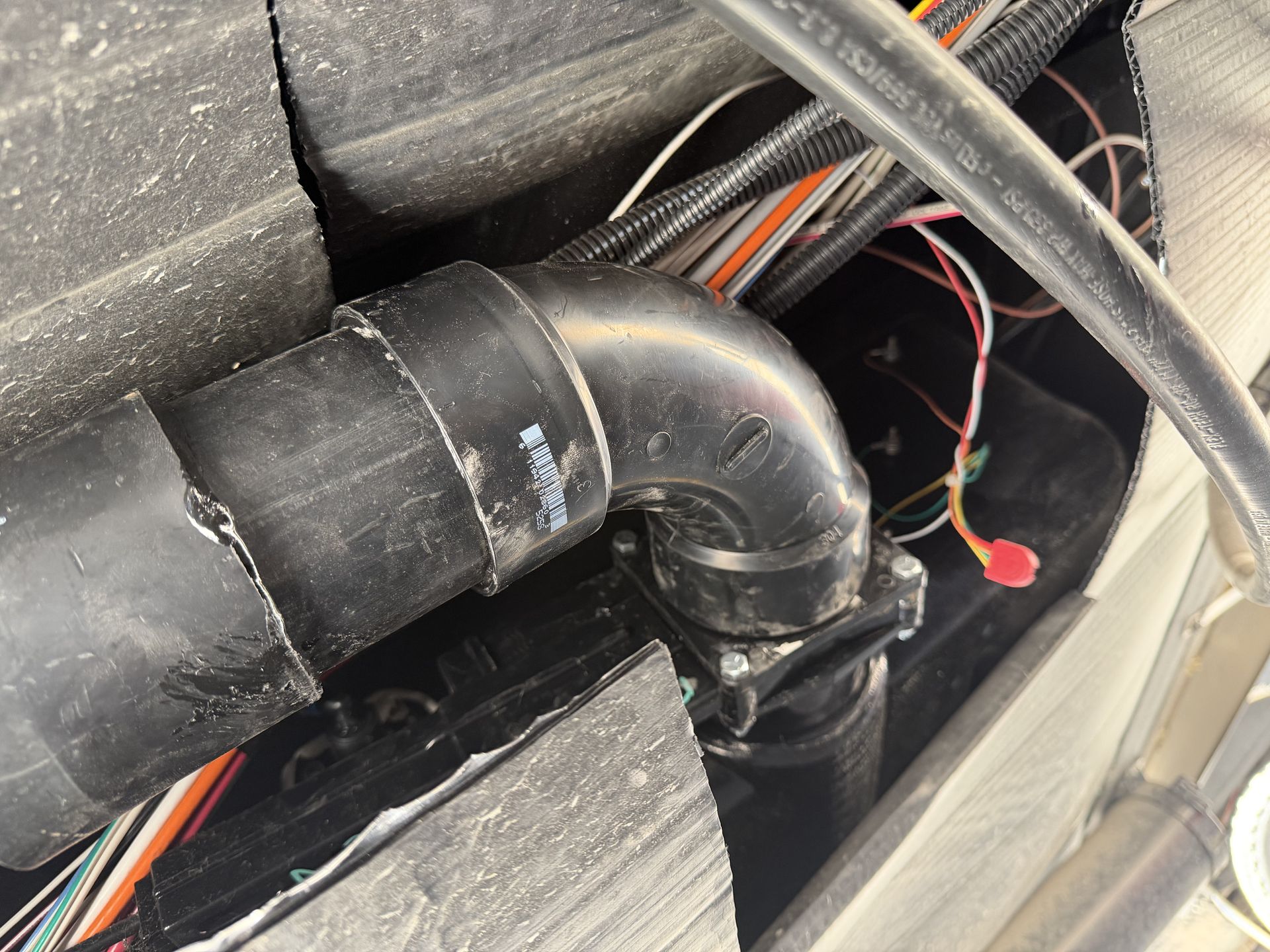 Newly installed black RV furnace exhaust elbow and pipe routed through insulation with wiring behind it
