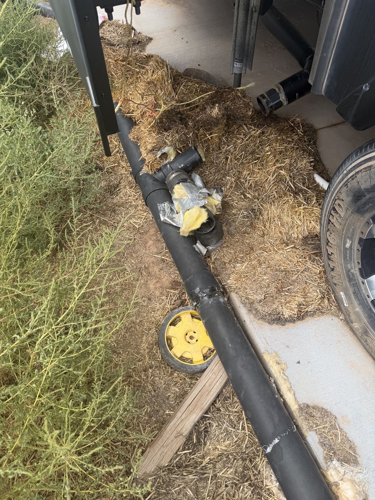 Black drain and LP lines routed along an RV chassis rail with a taped joint and insulation during an underbelly repair