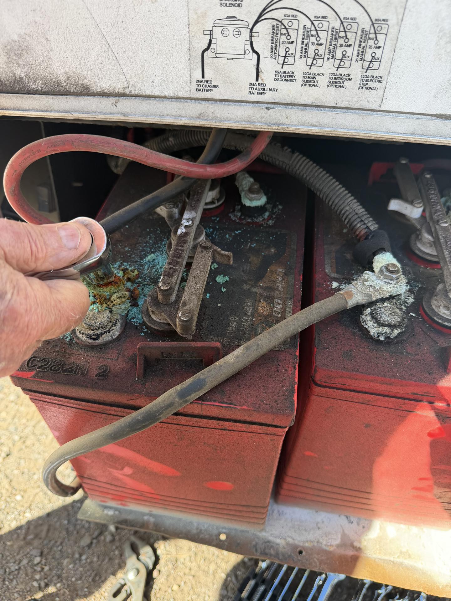 Technician using a wrench on a corroded RV battery terminal beside a second house battery with green corrosion on the posts
